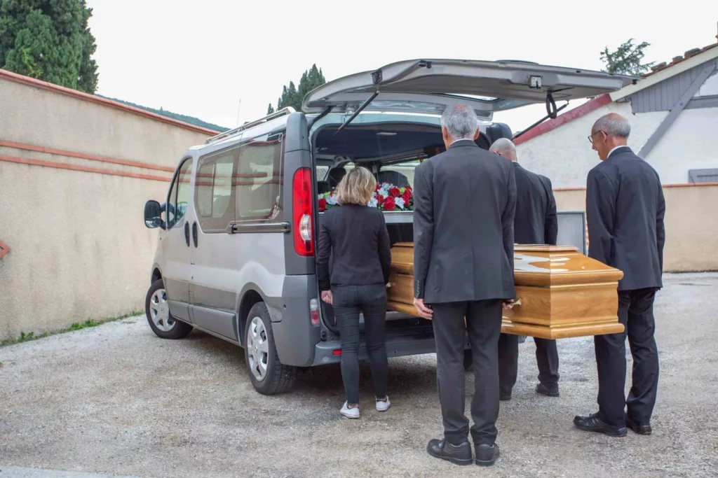Porteurs funéraires chargeant un cercueil en bois massif dans un véhicule de transport